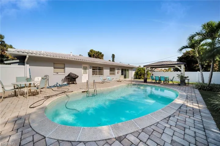 Private backyard oasis featuring a free-form swimming pool, extensive paver decking, and a dedicated covered gazebo area