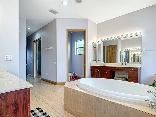 Bathroom featuring tile patterned flooring, vanity, and tiled bath