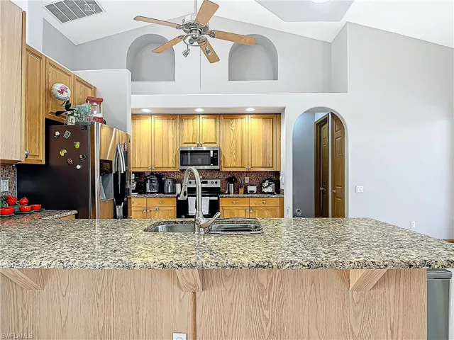 Kitchen with kitchen peninsula, appliances with stainless steel finishes, backsplash, sink, and high vaulted ceiling