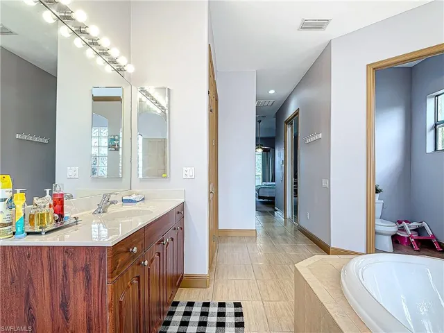 Bathroom featuring tile patterned flooring, vanity, toilet, and tiled bath