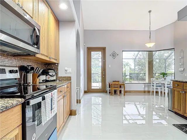 Kitchen with light stone countertops, appliances with stainless steel finishes, backsplash, and decorative light fixtures