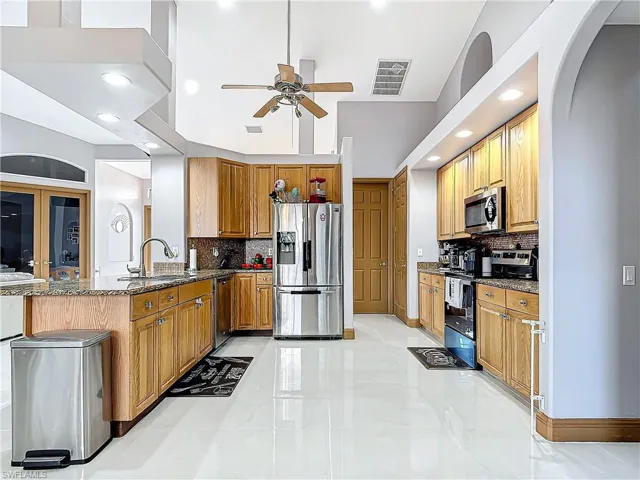 Kitchen featuring backsplash, stainless steel appliances, ceiling fan, sink, and stone counters