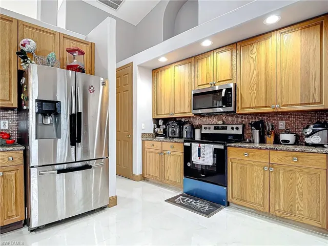 Kitchen featuring appliances with stainless steel finishes, a towering ceiling, tasteful backsplash, and light stone counters