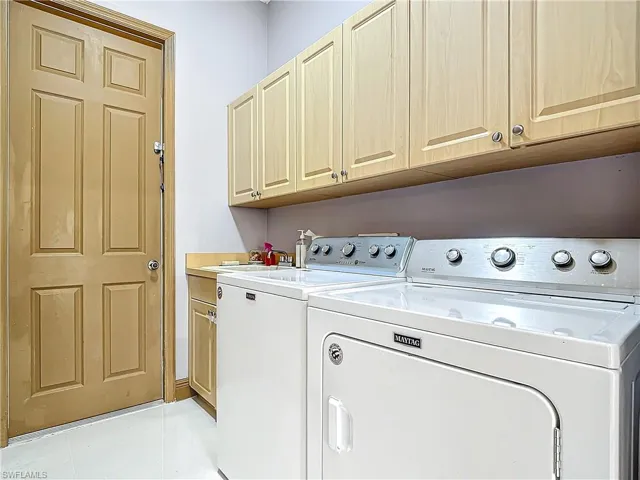 Clothes washing area with washing machine and clothes dryer, sink, light tile patterned flooring, and cabinets
