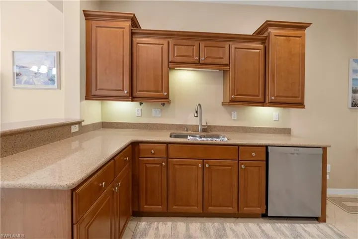 Kitchen featuring brown cabinets, dishwasher, and light stone counters