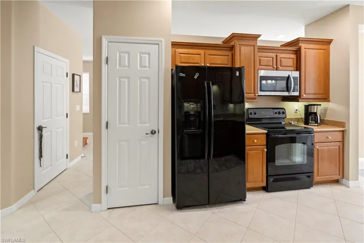 Kitchen featuring black appliances, light countertops, brown cabinetry, and light tile patterned floors