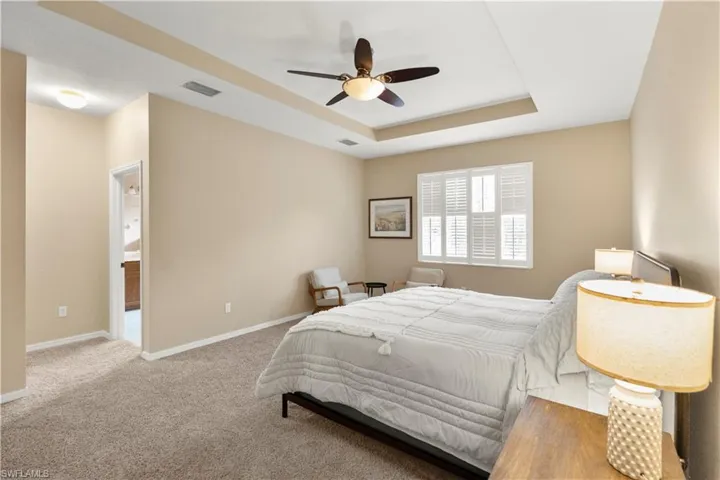 Bedroom featuring a tray ceiling, light carpet, and ceiling fan