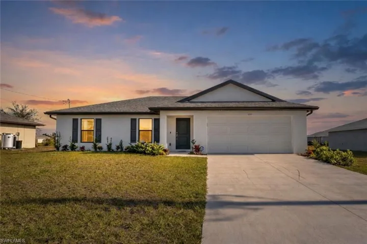 Ranch-style house with a garage, driveway, stucco siding, and a lawn