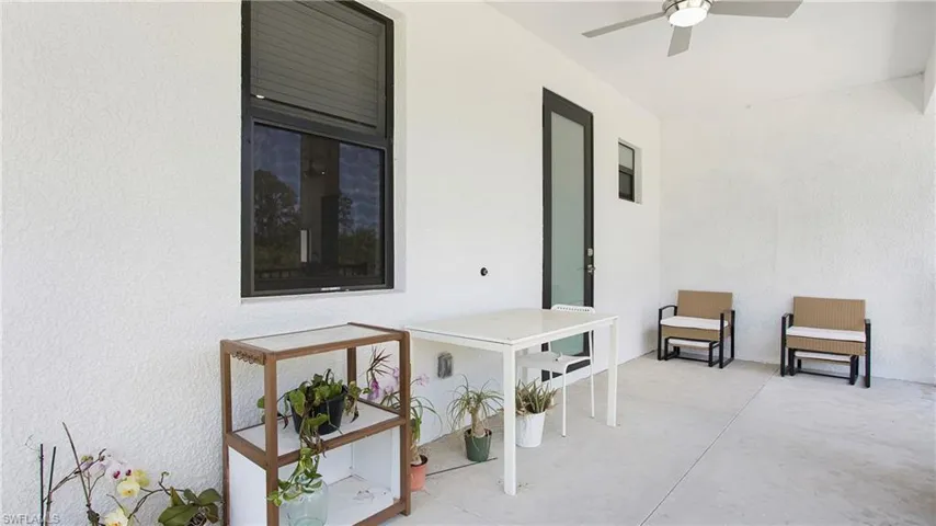 Outdoor patio space featuring a contemporary ceiling fan with integrated lighting, durable concrete flooring, and a dark-framed glass door