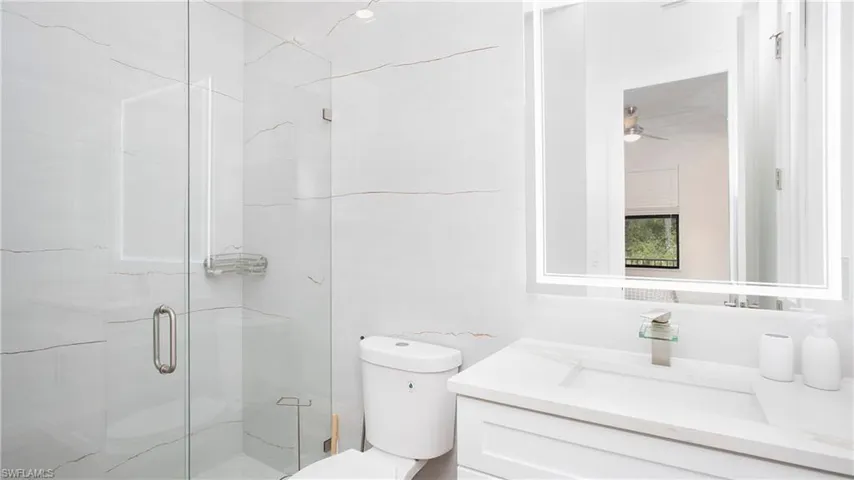 Bathroom featuring a glass-enclosed shower, white marble-look wall tiling, a modern vanity with integrated sink, a rectangular illuminated mirror, and a contemporary toilet