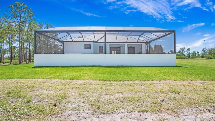 Rear exterior featuring a large screened lanai, a white concrete privacy wall, and a metal roof