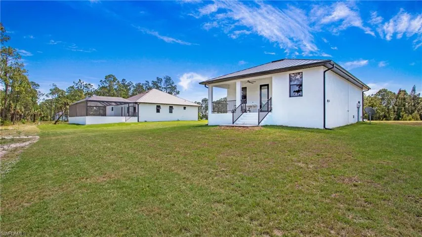 Expansive property featuring two structures, a screened enclosure, a covered porch with railings, and a large grassy area