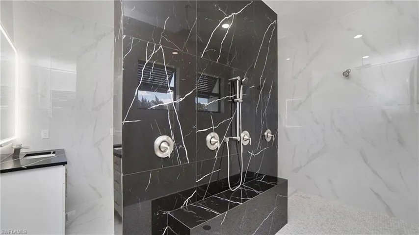 Luxurious shower featuring black marbled wall tiling with white veining, a built-in shower bench, and a brushed nickel shower system