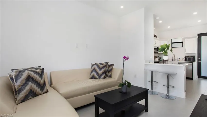 Open-concept living area featuring recessed lighting, a breakfast bar, stainless steel appliances, and a dark-framed glass paneled door
