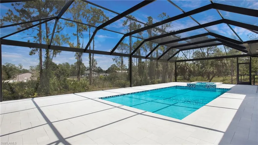 Expansive screened enclosure featuring a rectangular pool with an integrated spa, set against a backdrop of mature trees and open skies