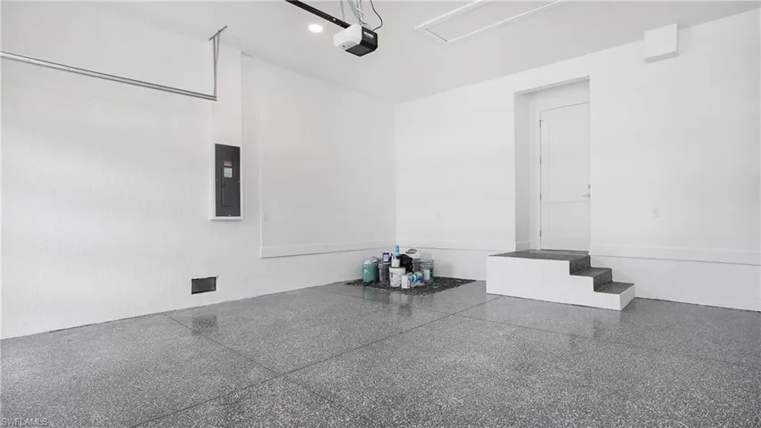 Spacious garage featuring a durable epoxy-coated concrete floor, bright white walls, a built-in step entry, and overhead garage door opener