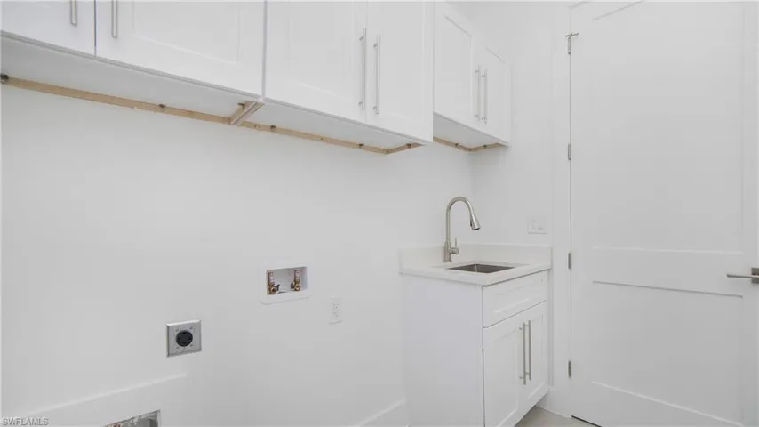 Laundry area featuring white cabinetry, a utility sink with a brushed nickel faucet, and a solid white door with brushed nickel hardware