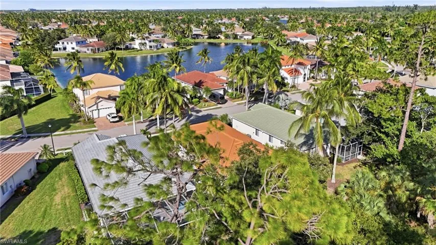 Aerial perspective of a residential neighborhood featuring paved streets, tropical palm trees, established landscaping, and a central community lake