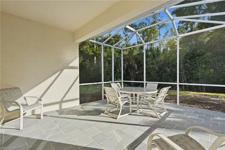 Screened-in lanai featuring tile flooring, metal frame construction, and a backdrop of mature trees