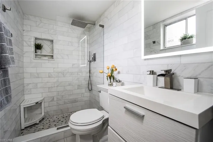 Bathroom featuring vanity, tasteful backsplash, a tile shower, tile walls, and toilet