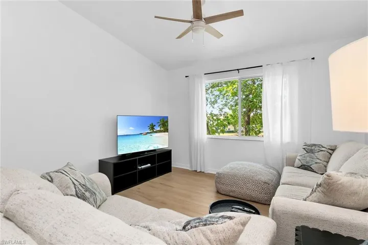 Living area featuring wood finished floors, vaulted ceiling, ceiling fan, and baseboards