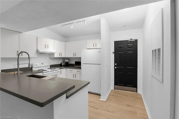 Kitchen with white appliances, under cabinet range hood, dark countertops, rail lighting, and a peninsula