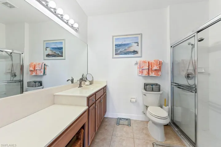 Bathroom featuring a shower with door, vanity, toilet, and tile patterned flooring