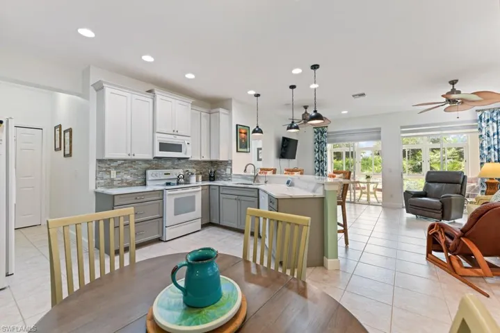 Kitchen with gray cabinetry, white appliances, pendant lighting, kitchen peninsula, and decorative backsplash