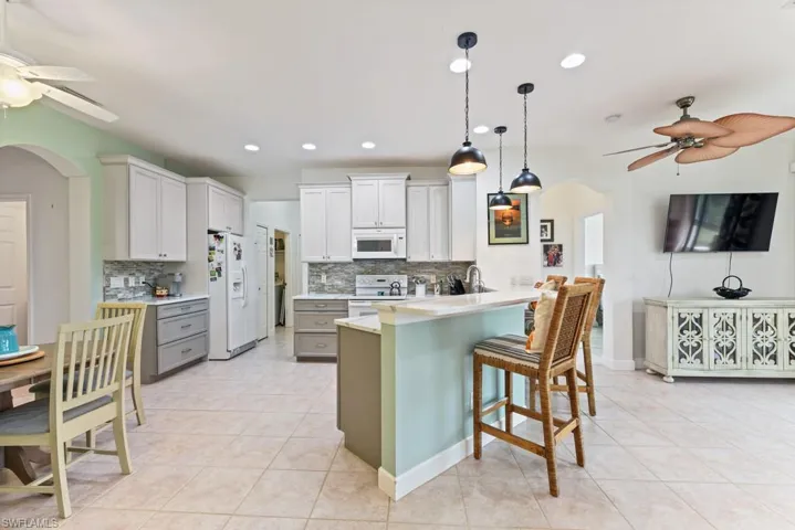 Kitchen with white appliances, light tile patterned floors, ceiling fan, decorative backsplash, and a breakfast bar