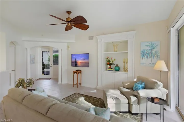 Tiled living area with built in shelves, ceiling fan, and arched walkways