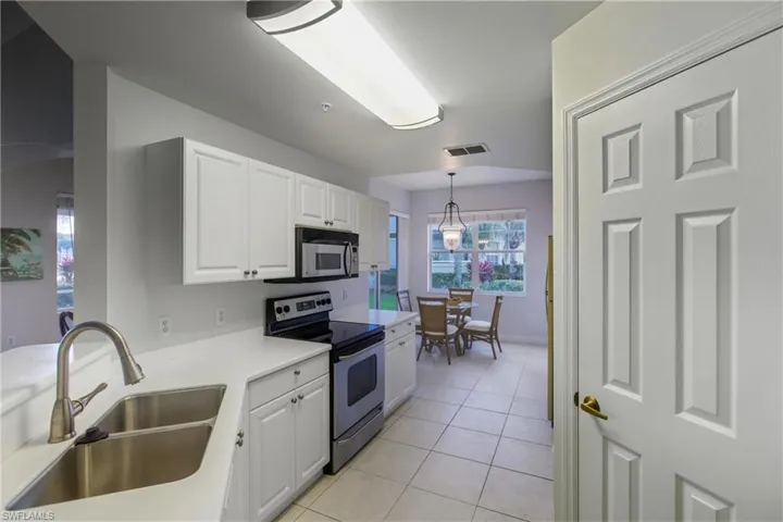Kitchen with stainless steel electric stove, light countertops, white cabinetry, light tile patterned floors, and pendant lighting