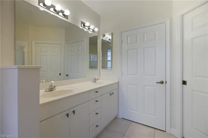 Bathroom with double vanity, light tile patterned floors, and an enclosed shower