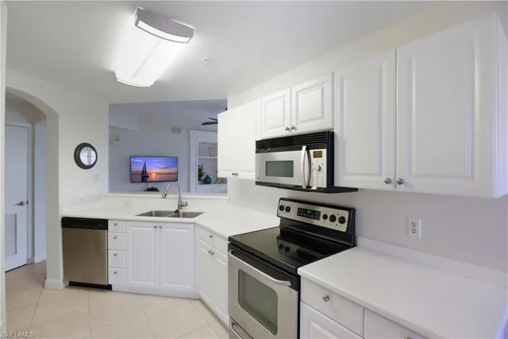 Kitchen featuring appliances with stainless steel finishes, white cabinets, arched walkways, and light countertops