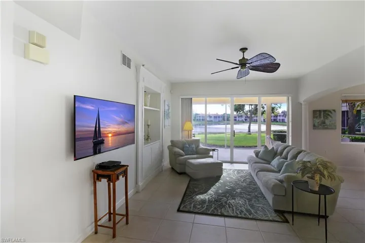 Living area with light tile patterned flooring, arched walkways, ceiling fan, and built in shelves