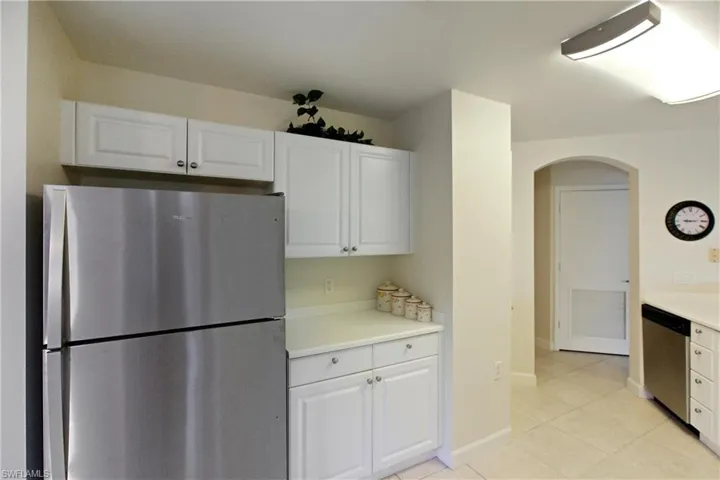 Kitchen featuring appliances with stainless steel finishes, light countertops, arched walkways, white cabinets, and light tile patterned flooring