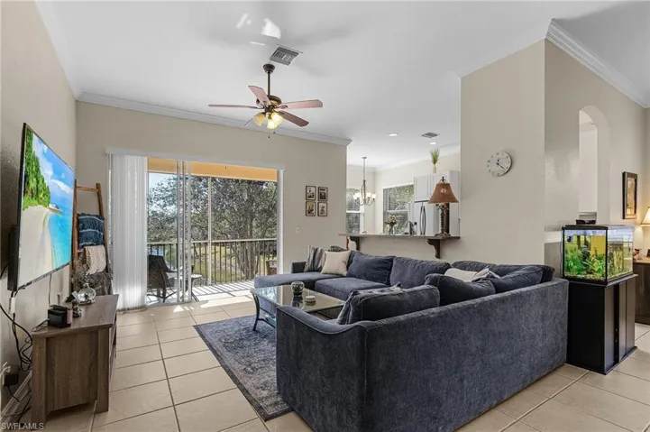 Living room with light tile patterned floors, ceiling fan with notable chandelier, and ornamental molding