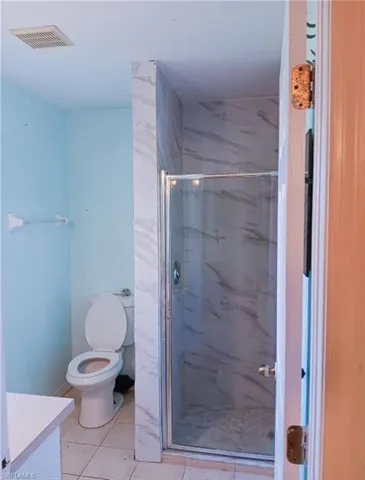 Bathroom with a shower with door, vanity, toilet, and tile patterned floors