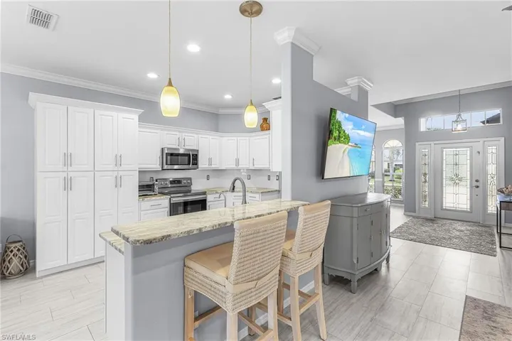 Kitchen with crown molding, stainless steel appliances, a kitchen bar, white cabinetry, and pendant lighting