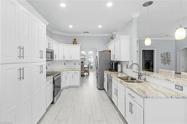 Kitchen featuring arched walkways, a peninsula, a breakfast bar area, light stone countertops, and crown molding