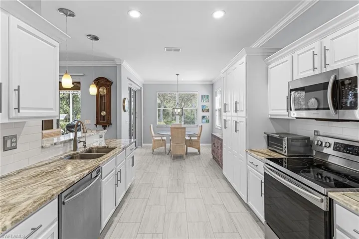 Kitchen featuring decorative backsplash, stainless steel appliances, white cabinets, ornamental molding, and light stone countertops