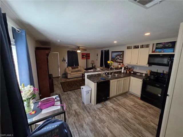 Kitchen featuring a peninsula, black appliances, open floor plan, wood finished floors, and a ceiling fan