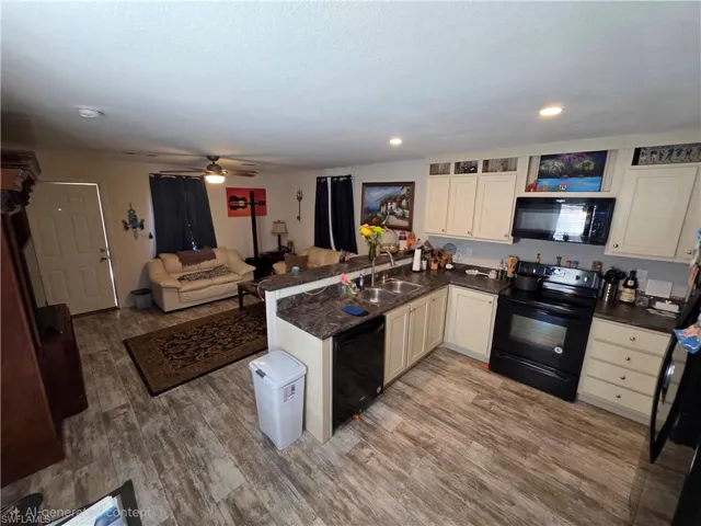 Kitchen with a peninsula, black appliances, open floor plan, a ceiling fan, and wood finished floors