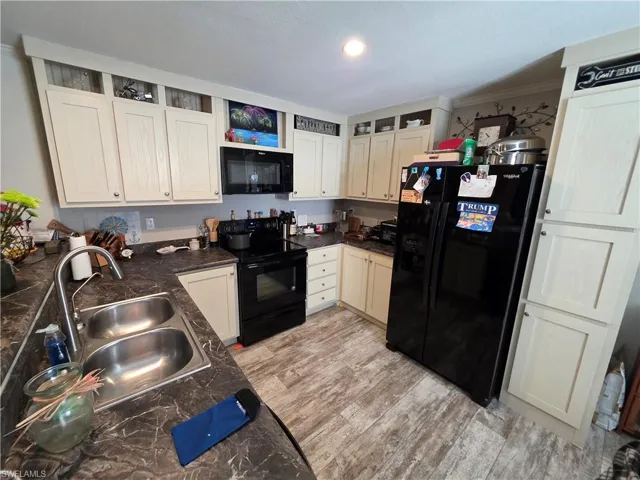 Kitchen with black appliances, light wood-style floors, open shelves, ornamental molding, and dark stone countertops