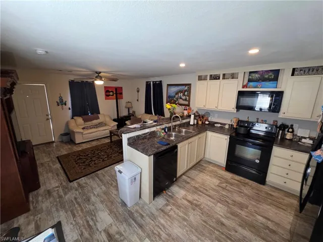 Kitchen with a peninsula, black appliances, a ceiling fan, open floor plan, and light wood-style flooring