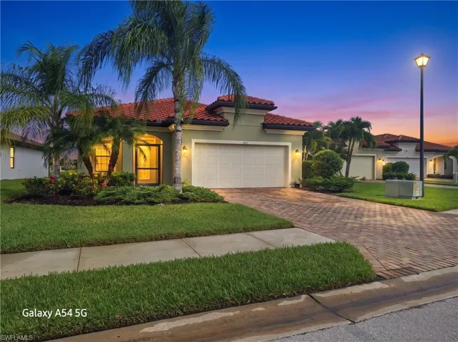 Mediterranean-style exterior featuring a multi-gabled clay tile roof, herringbone-pattern paver driveway, two-car garage, and established landscaping with palm trees