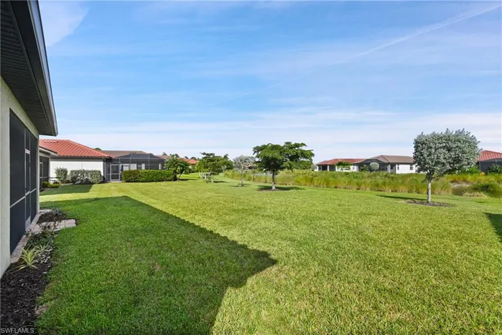 Backyard featuring a large grass lawn, mature trees, and a screened-in covered patio