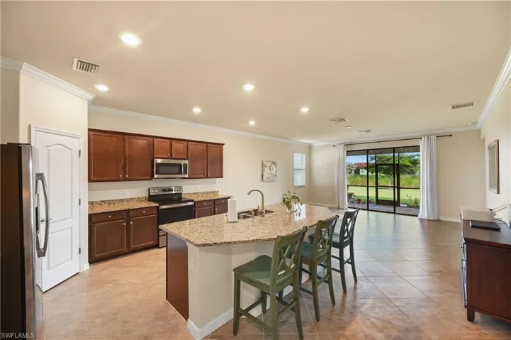 Kitchen featuring cherry-finish cabinetry, stone-style countertops, stainless steel appliances, a central island with a double-basin sink, and tile flooring