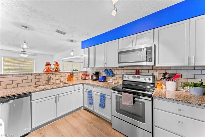 Kitchen with white cabinets, hanging light fixtures, stainless steel appliances, and sink