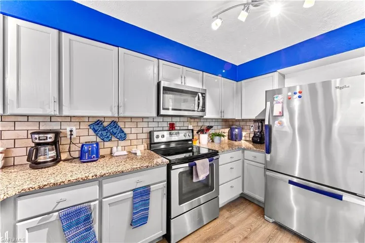 Kitchen with light stone countertops, appliances with stainless steel finishes, light hardwood / wood-style flooring, and white cabinets