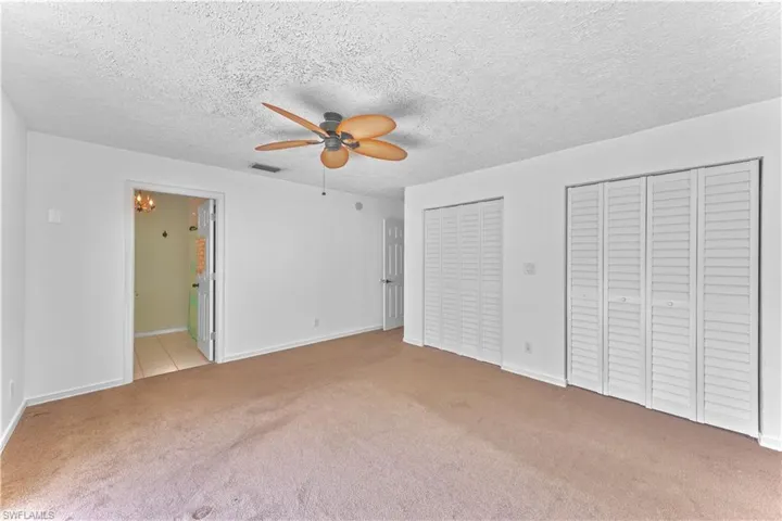 Unfurnished bedroom with ceiling fan, a textured ceiling, multiple closets, ensuite bathroom, and light colored carpet
